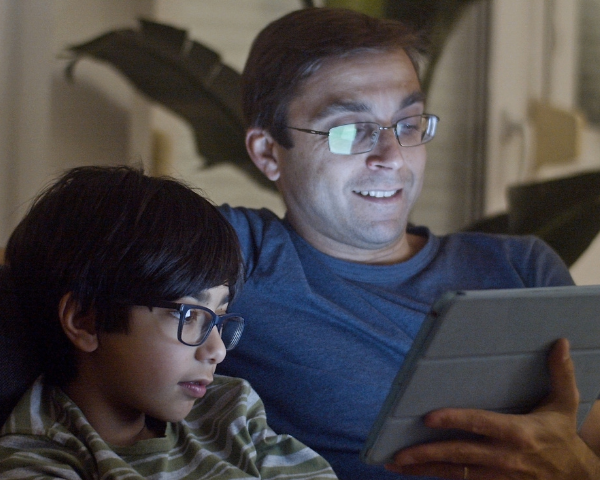 father and son wearing glasses, looking at a tablet