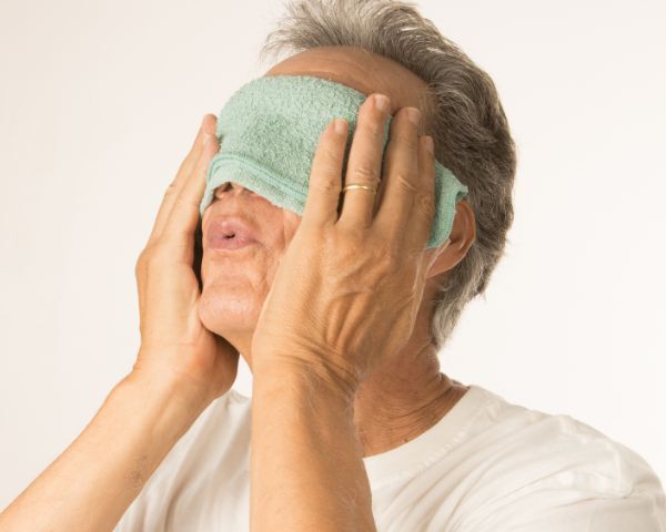 a man holding a warm compress over his eyes