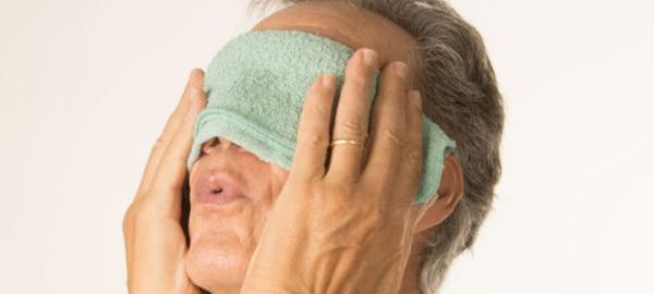 a man holding a warm compress over his eyes