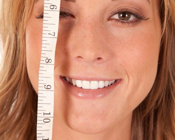 close up of a woman smiling and holding a measuring tape near her face