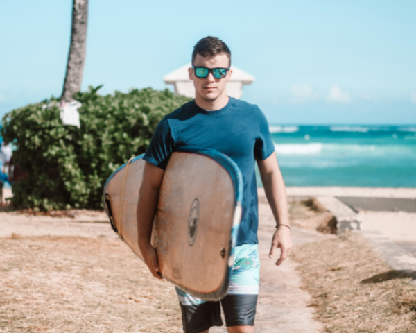 surfing athlete on the beach carrying a surf board and wearing sports sunglasses