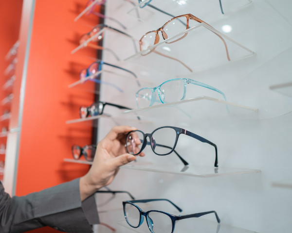 A person's hand reaching for a pair of eyeglasses from a display shelf.