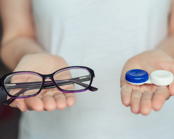 One hand holding a pair of glasses, one hand holding a contact lens case