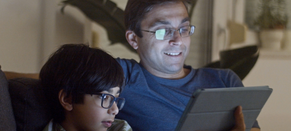 father and son wearing glasses, looking at a tablet.