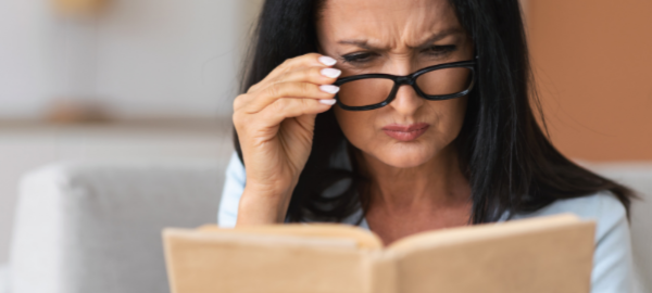 woman struggling to read a book with reading glasses