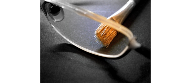 Close up photo of paint brush being used to clean glasses lenses