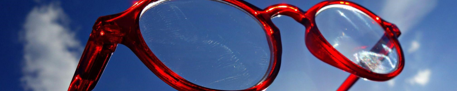 Red glasses held up in the light showing scratched lenses
