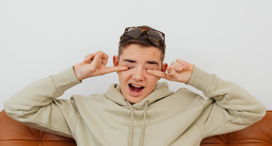 A boy rubbing his eyes while wearing glasses on top of his head