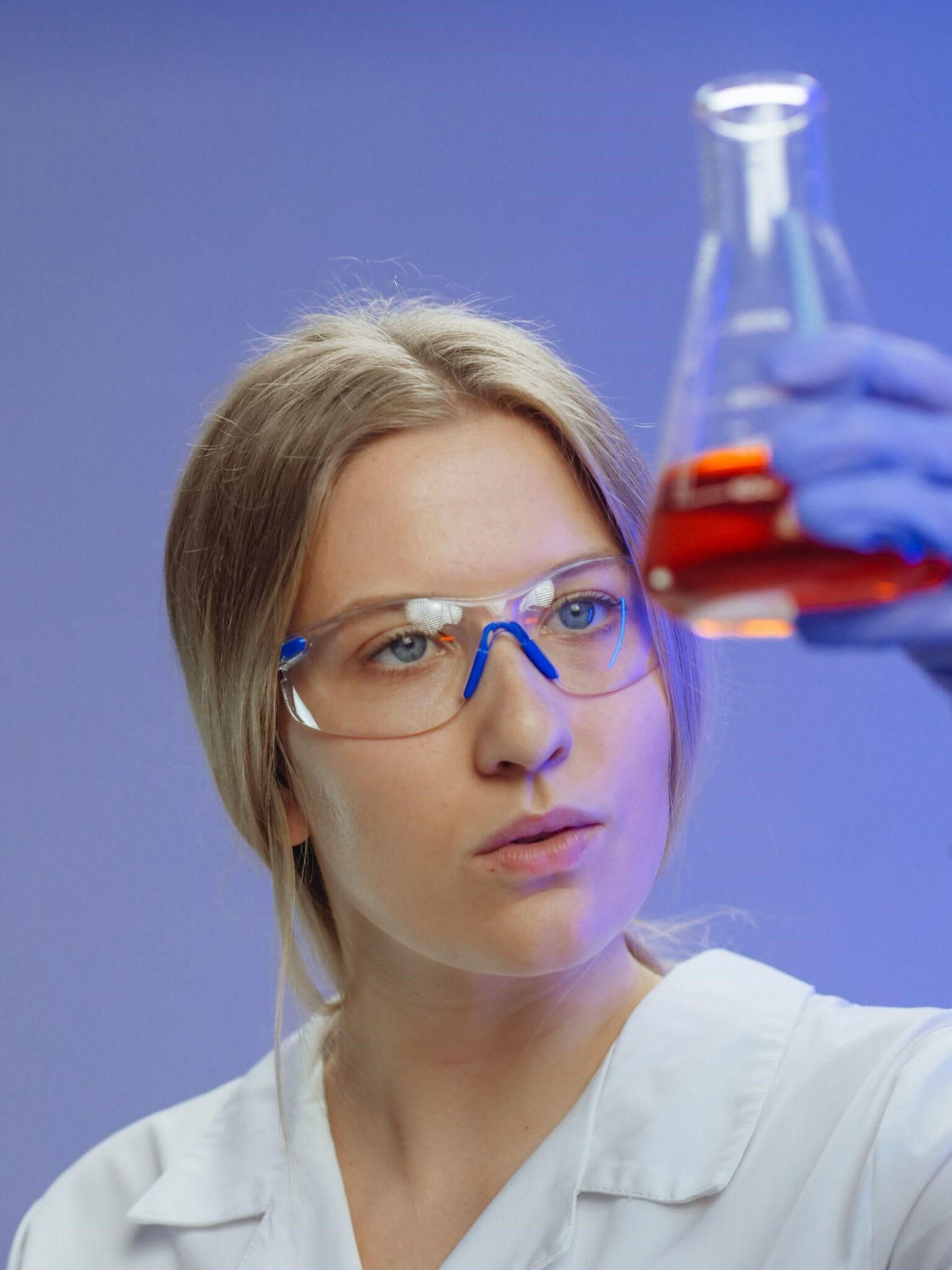 A girl wearing safety glasses while holding a glass flask
