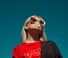 model wearing bright colored sunglasses and tshirt with flower petal in her mouth