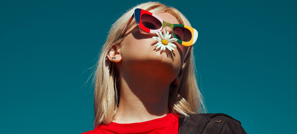 Woman wearing colourful sunglasses with a flower in her mouth