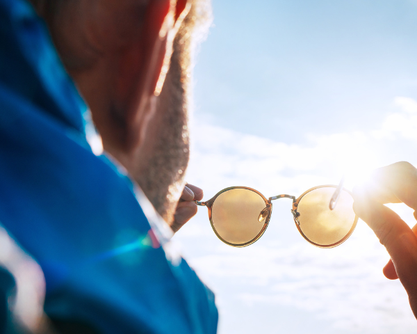 man holding sunglasses towards the sun