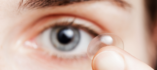 In focus contact lens on a finger tip with an eye in the background
