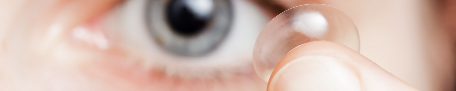 In focus contact lens on a fingertip with an eye in the background