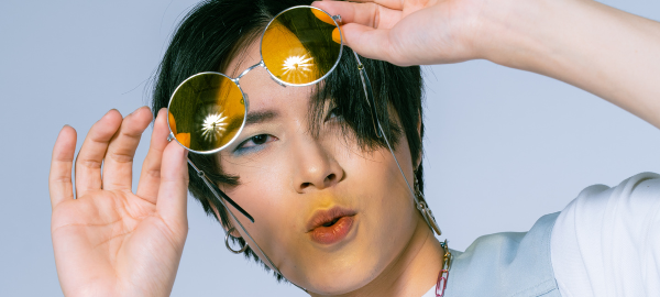 Asian guy with blue eyeshadow holding a pair of yellow lens sunglasses