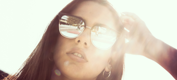 Close up woman wearing mirrored sunglasses with the sun behind her