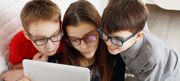 3 kids huddled around a tablet with glasses on